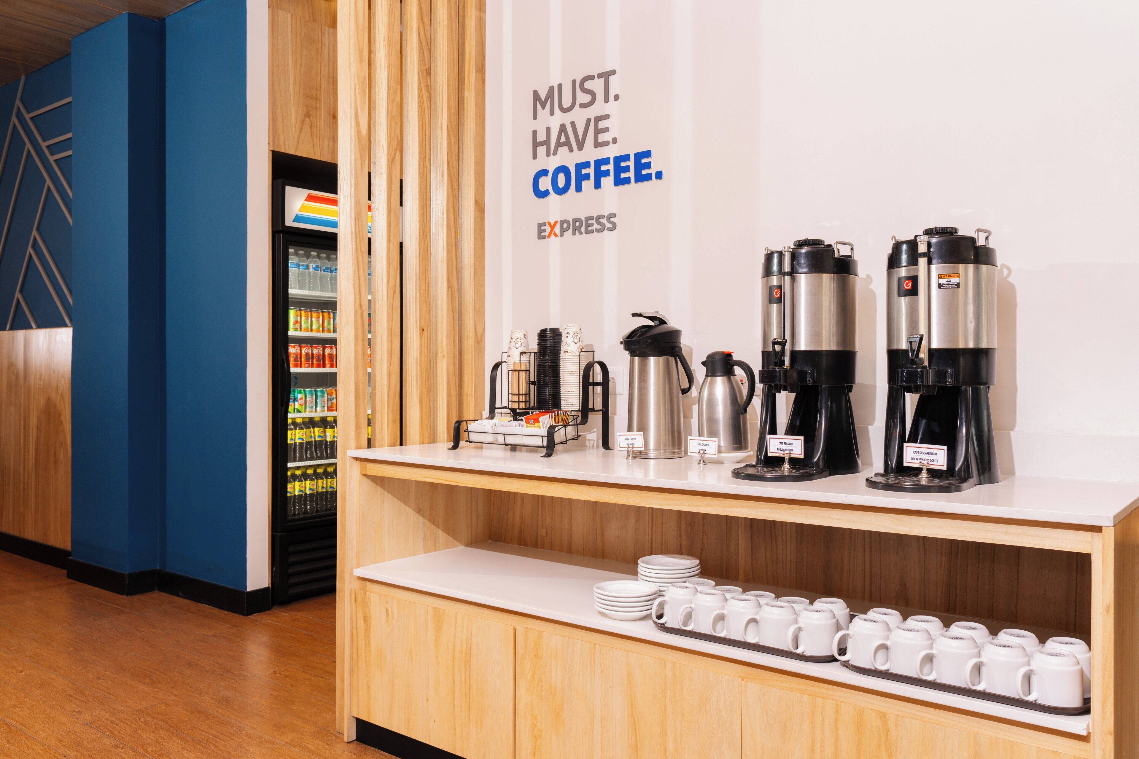 A coffee station with multiple coffee makers and a refrigerator stocked with beverages.