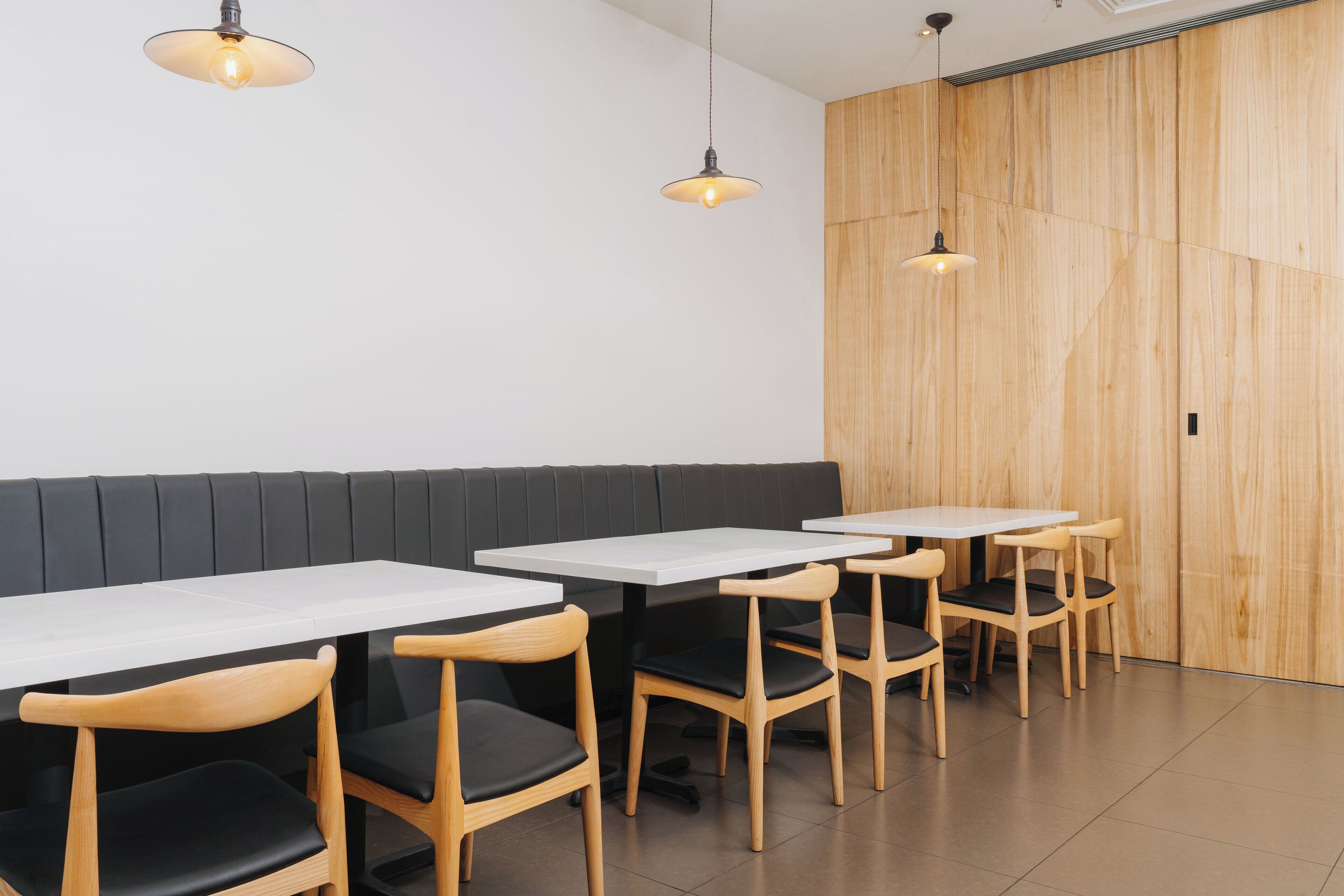 A restaurant interior with wooden panel walls, black cushioned booths, and white tables.