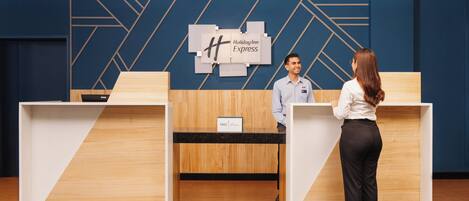 A reception desk with a Holiday Inn Express sign, a wooden reception desk, and a blue geometric wall design.