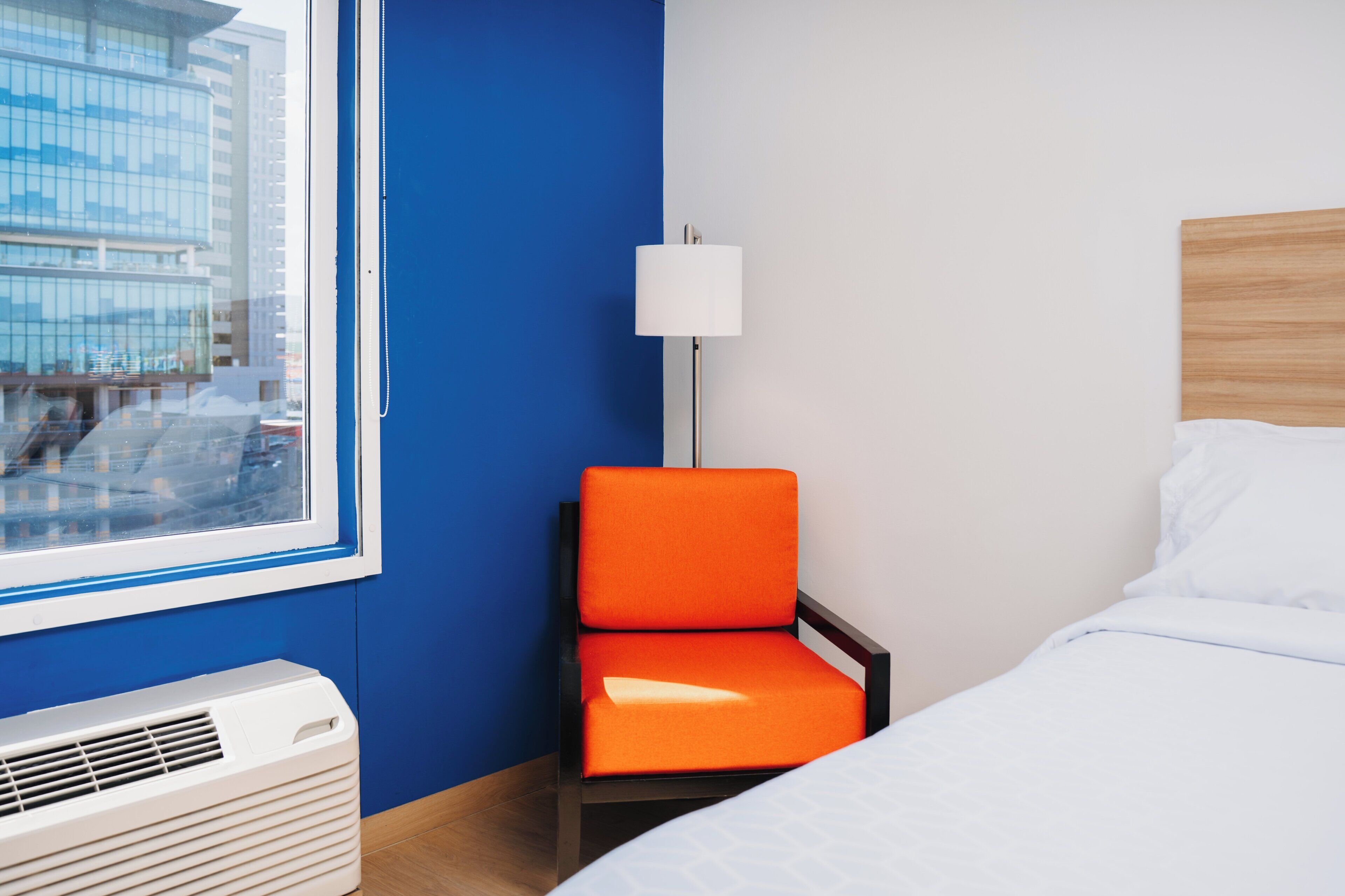 Une chambre d’hôtel avec un lit, une chaise, une lampe et un climatiseur.