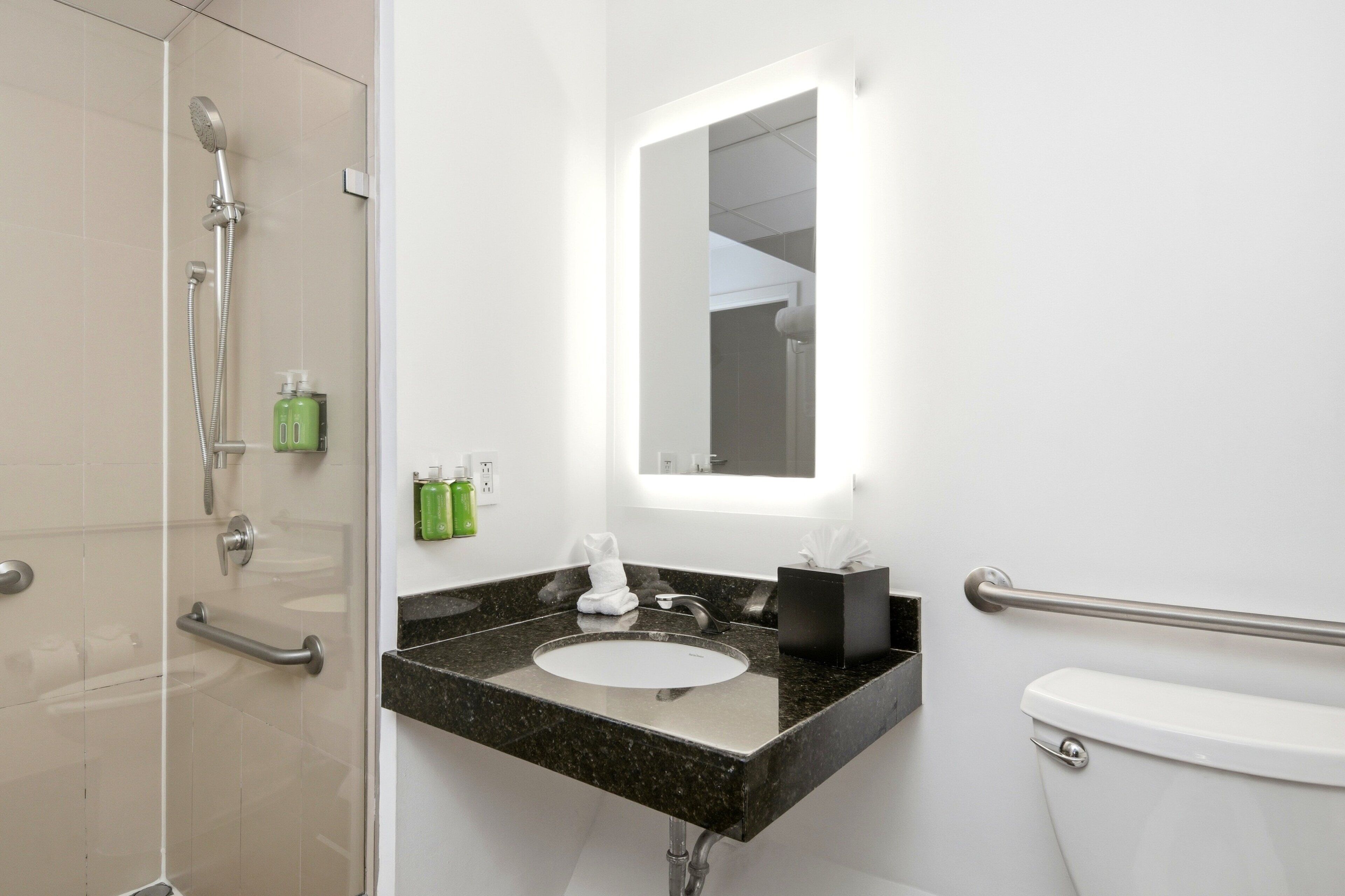 Un baño con ducha, lavabo, inodoro y un espejo con luz.