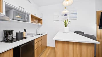 Una cocina moderna con microondas, cafetera y pileta. Se aprecia un armario de madera y una encimera blanca.