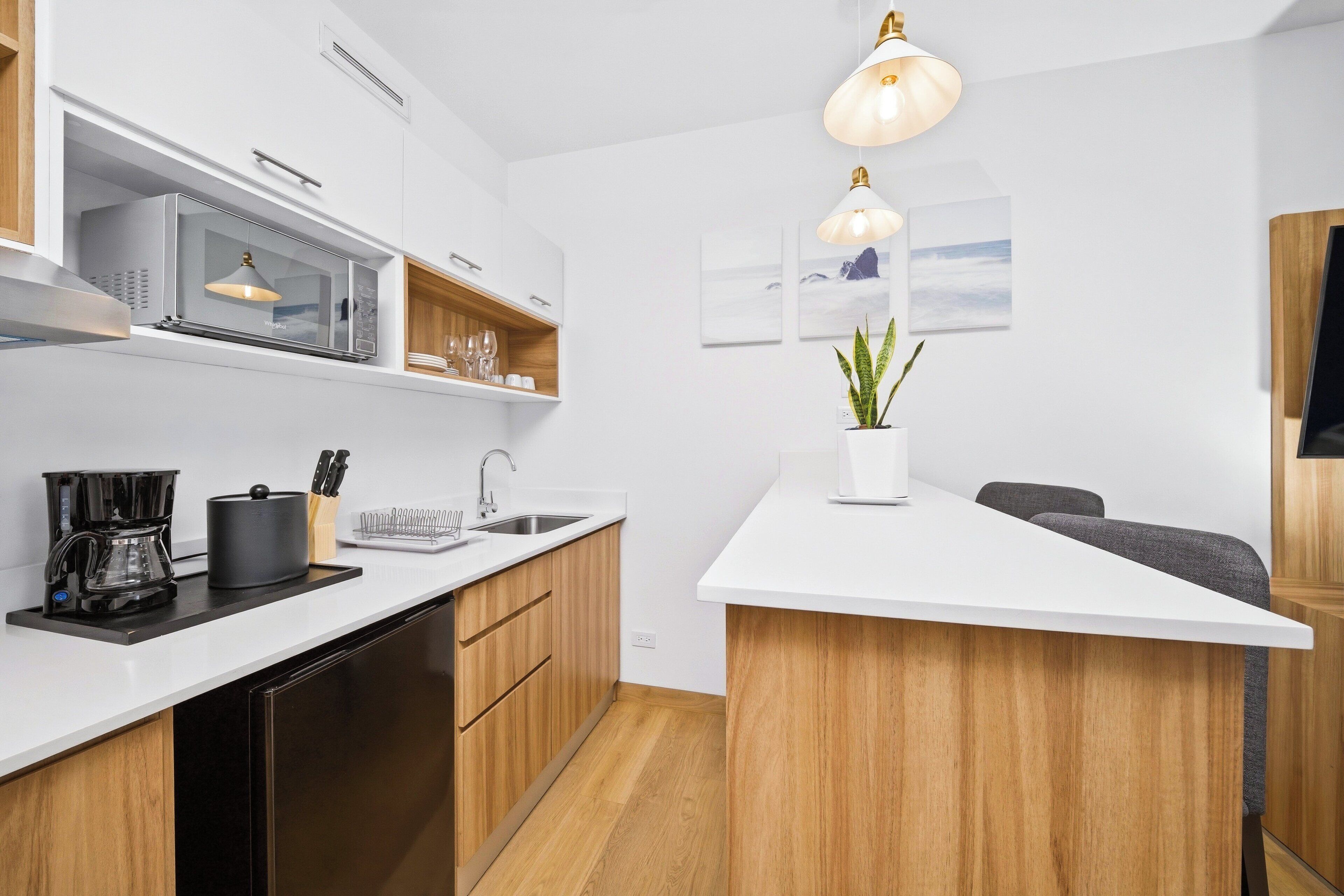A modern kitchen with a microwave, coffee maker, and wooden cabinets.