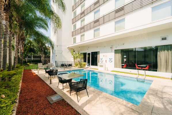 A swimming pool with a tiled deck, surrounded by palm trees and a building with balconies. - Holiday Inn Express Tegucigalpa by IHG (Tegucigalpa)