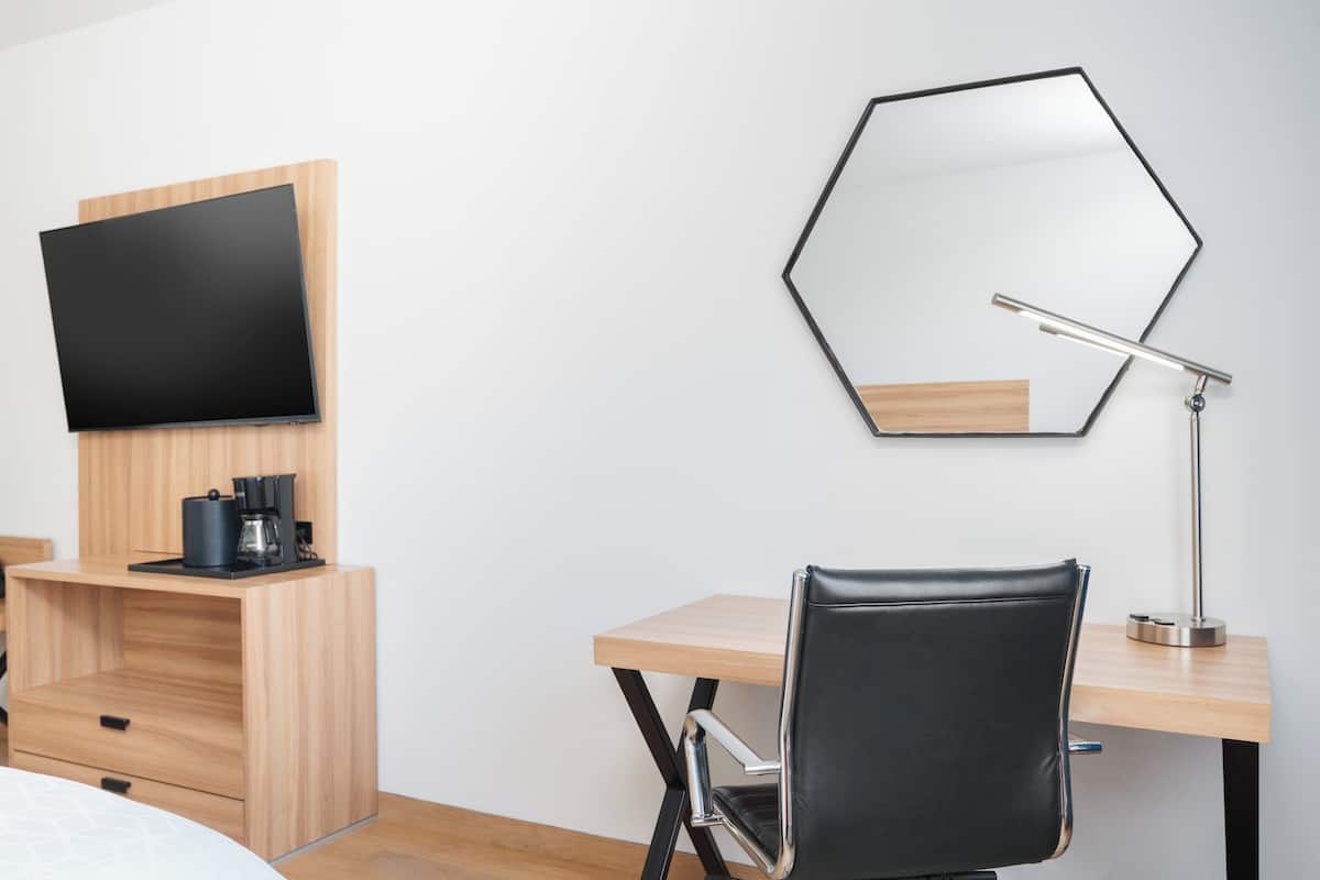A hotel room with a bed, a desk with a chair, a TV, a coffee maker, and a mirror.