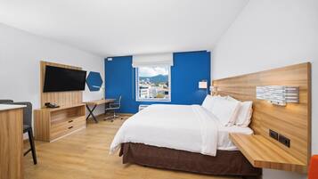Una habitación de hotel moderna con cama, escritorio, silla, televisión y ventana con vista a la ciudad.
