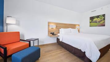 A hotel room with a bed, a nightstand, a lamp, a chair, and a bench.