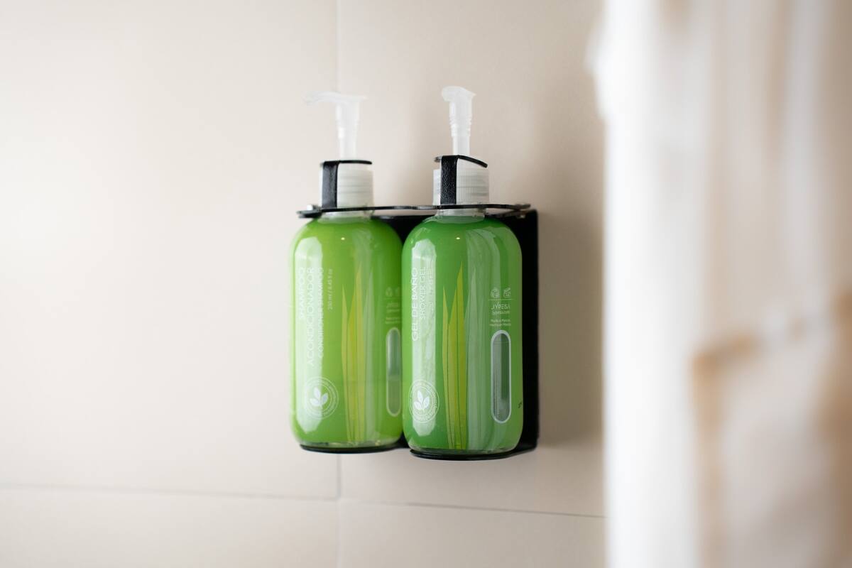 Two green bottles with pumps on a white tiled wall.