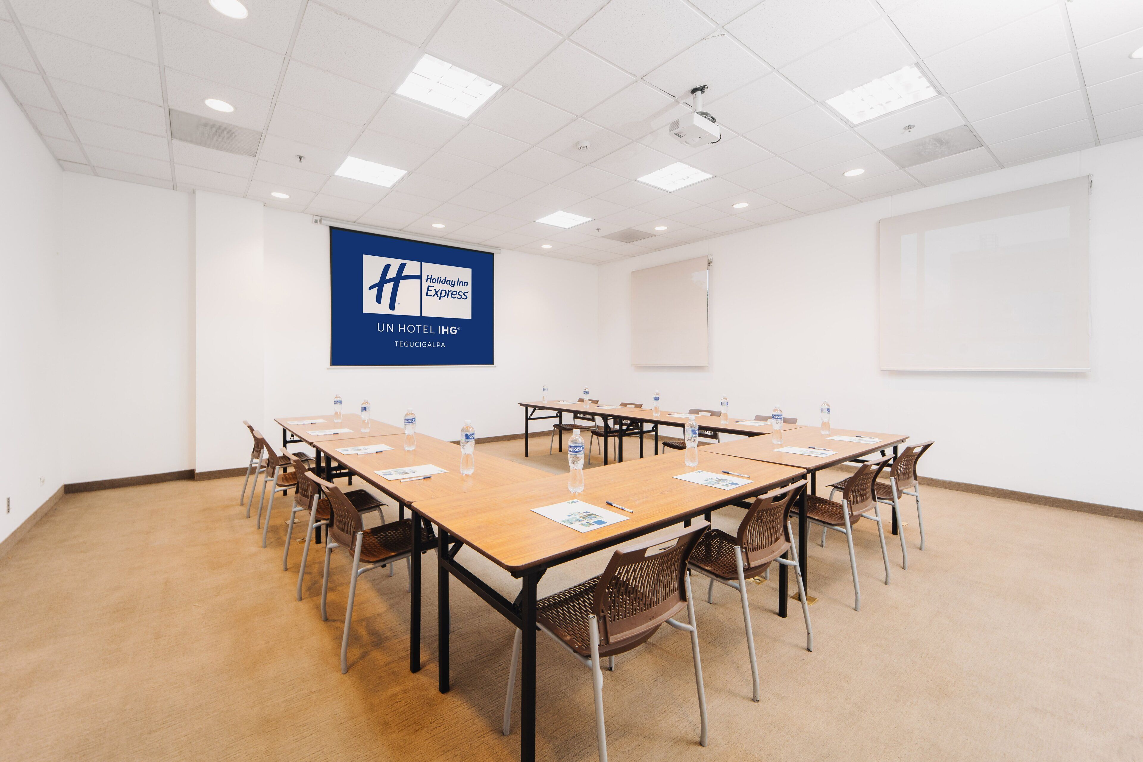 A conference room with a large table, chairs, a projector screen, and a banner for Holiday Inn Express.