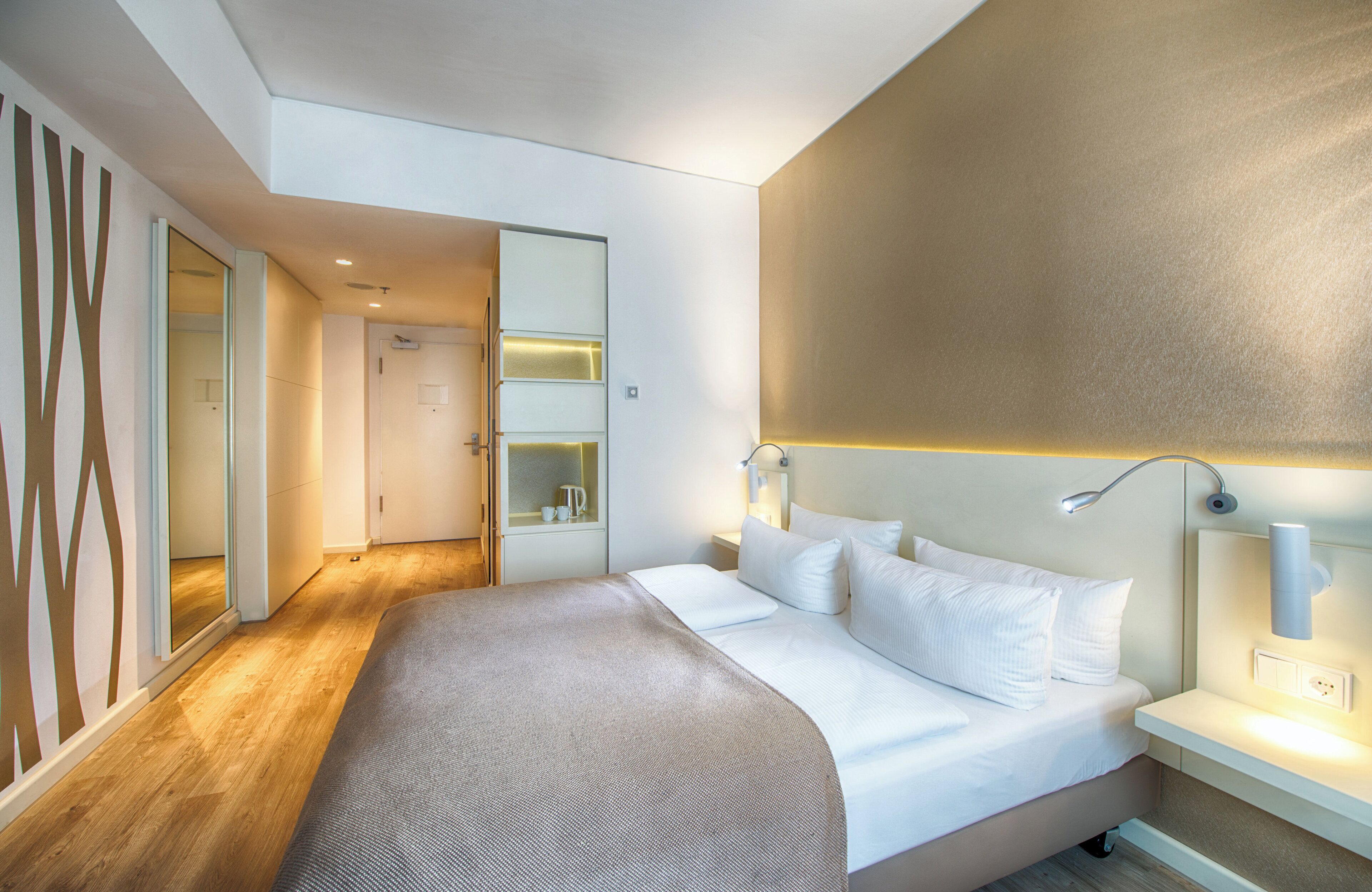 A modern hotel room with a large bed, bedside tables, a mirror, and a walk-in closet.