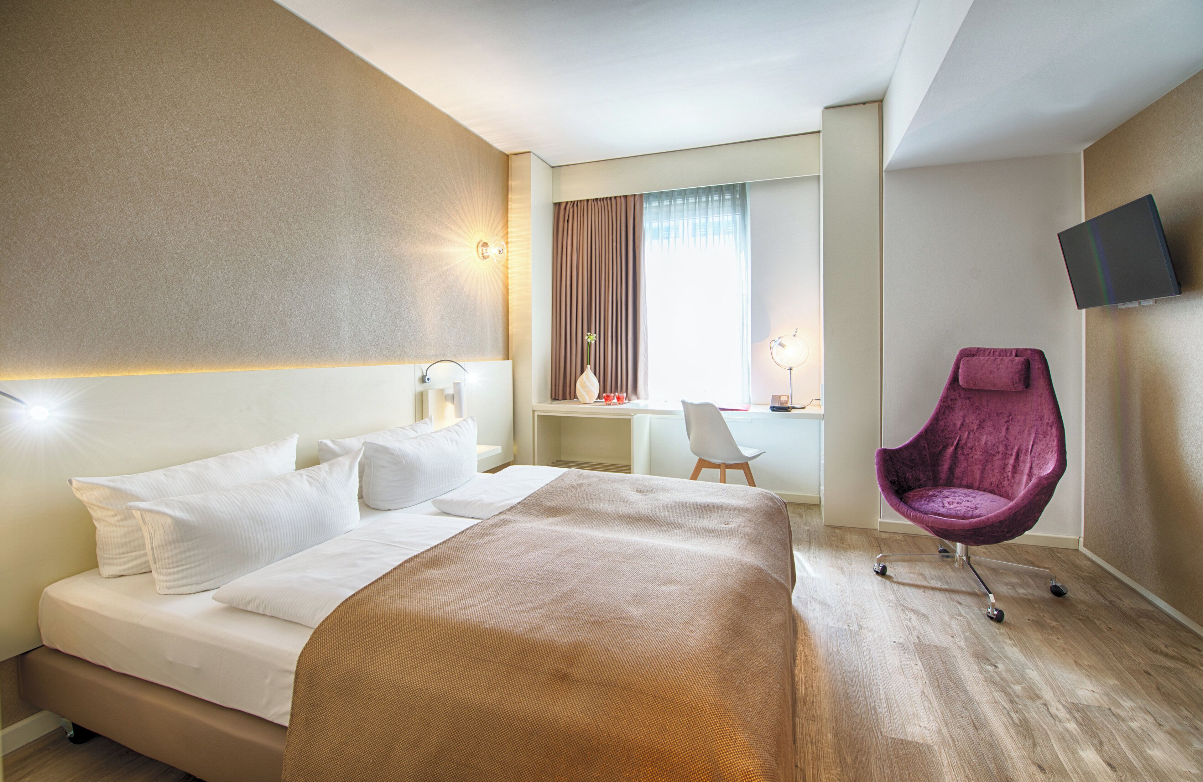Habitació d'hotel amb llit, escriptori, cadira i televisió.