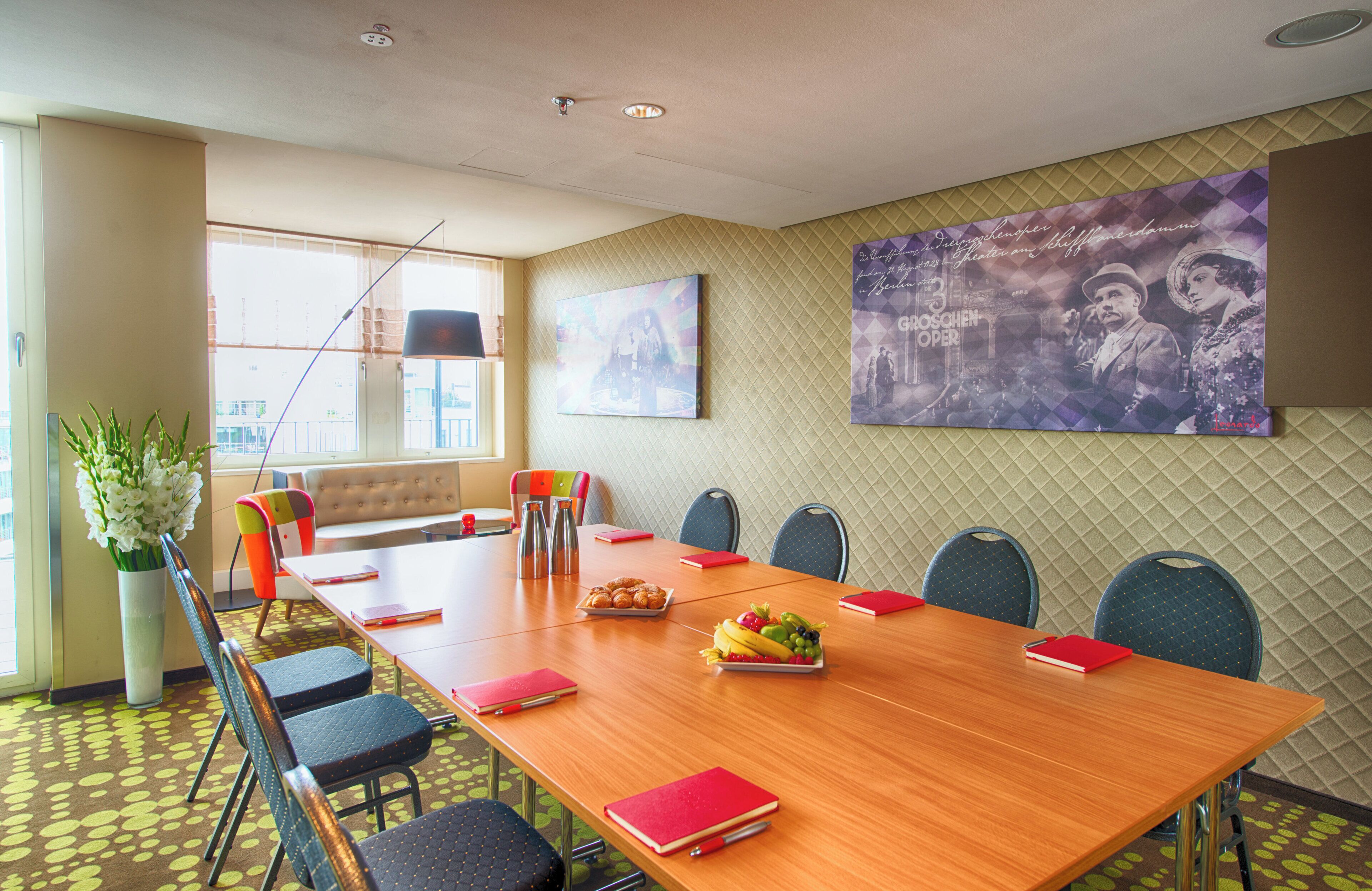 A conference room with a long table, multiple chairs, a potted plant, and artwork on the walls.