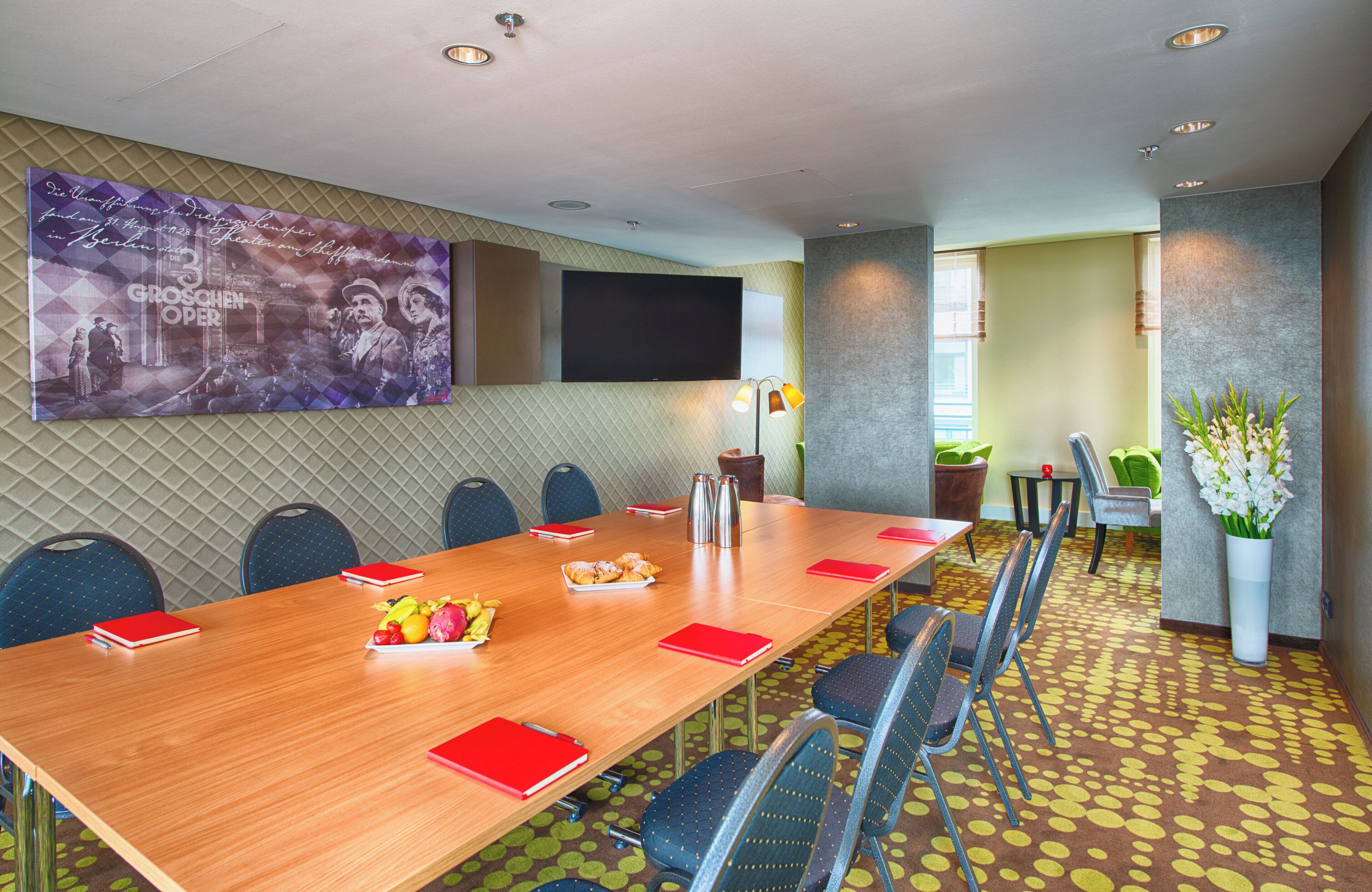 A conference room with a long table, chairs, a large poster, and a TV on the wall.
