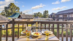 A balcony with a table set for breakfast, including plates of fruit and pastries, and a bottle of champagne. - The Sebel Swan Valley The Vines (The Vines)