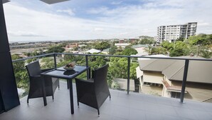 Een balkon met rieten stoelen en een tafel, met uitzicht op een woongebied met gebouwen en groen.