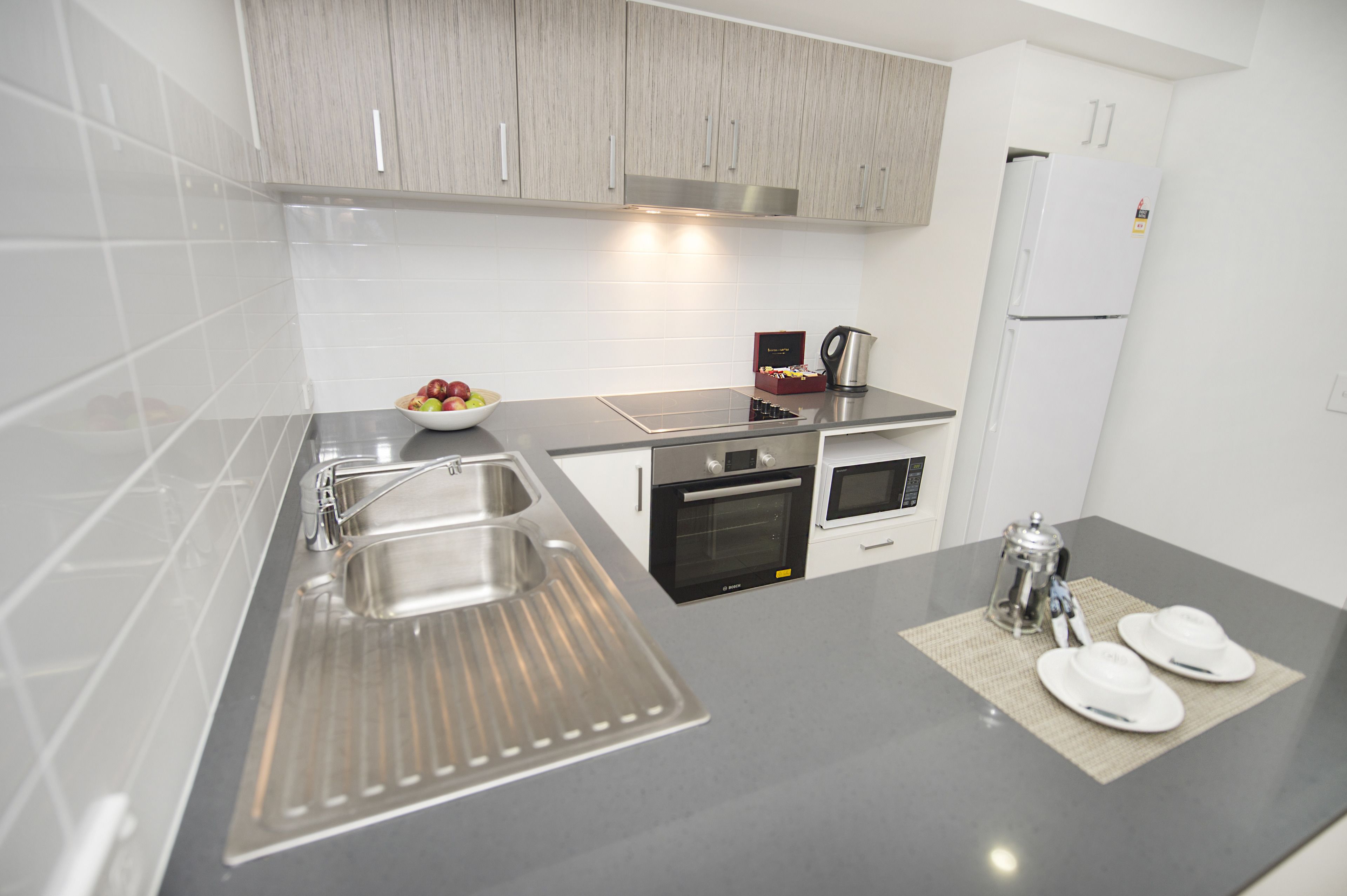 A modern kitchen with a stainless steel sink, two ovens, a coffee maker, and a refrigerator.