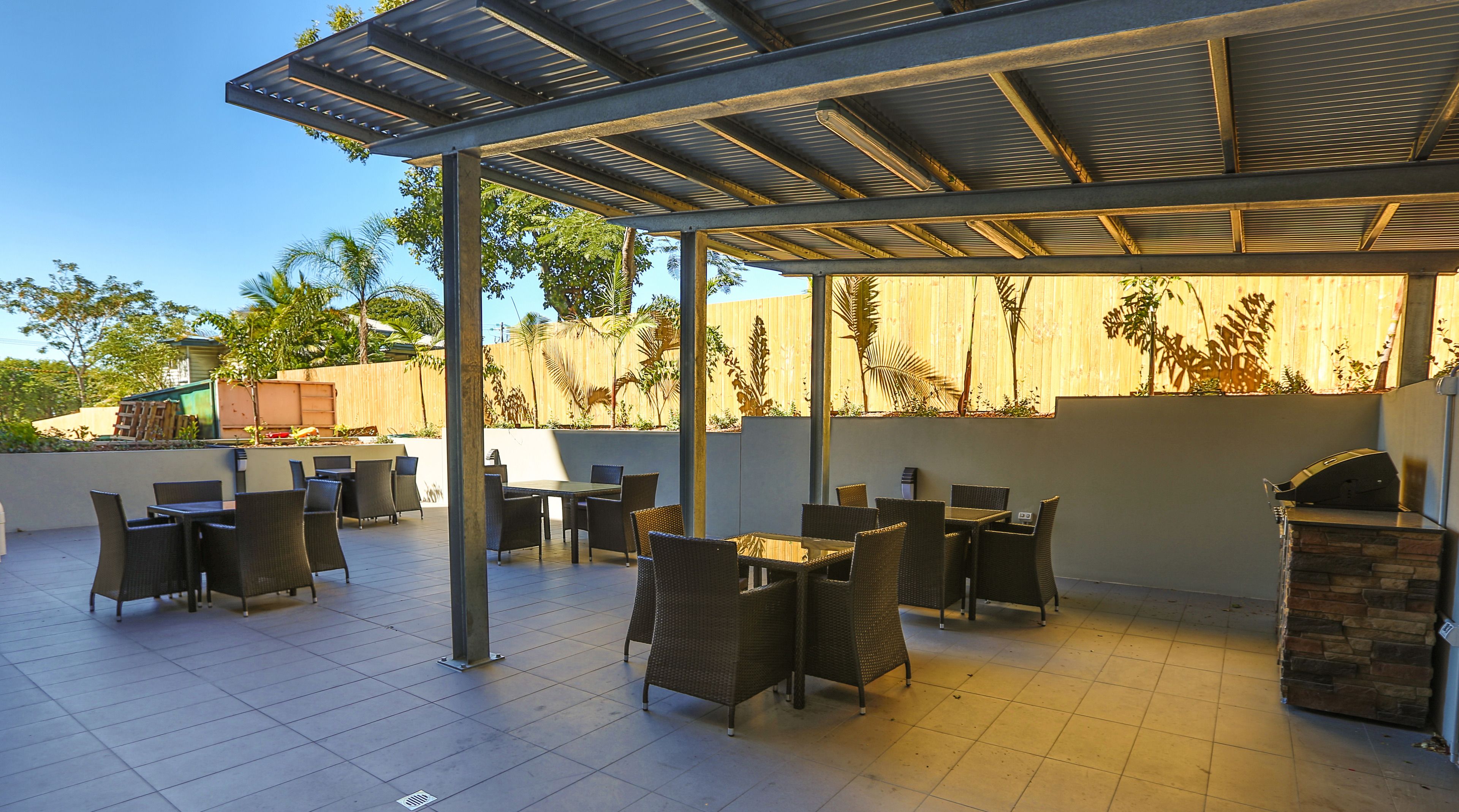 Un patio al aire libre con suelo de baldosas, zonas de estar cubiertas y una parrilla de barbacoa.