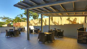 Un patio al aire libre con suelo de baldosas, zonas de estar cubiertas y una parrilla de barbacoa.