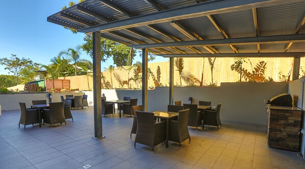 Un patio al aire libre con suelo de baldosas, zonas de estar cubiertas y una parrilla de barbacoa.