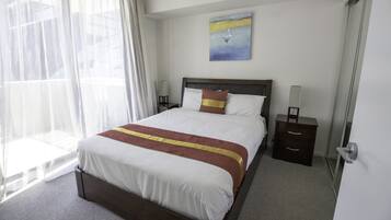 A neatly made bed with a brown headboard, a bedside table with a lamp, and a painting on the wall.