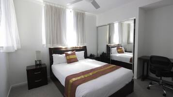 A hotel room with a large bed, a desk, a chair, a nightstand, and a ceiling fan.