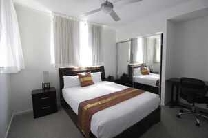 A hotel room with a large bed, a desk, a chair, a nightstand, and a ceiling fan.