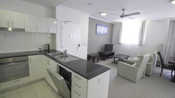 A modern kitchen with white cabinets, a black countertop, and a built-in dishwasher. There is a dining area with a table and chairs, and a ceiling fan.