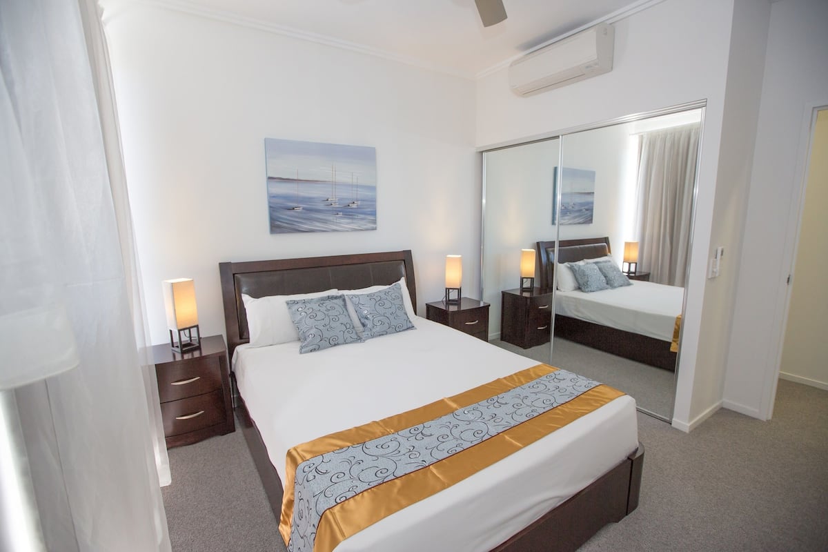 Een hotelkamer met een groot bed, een nachtkastje met een lamp, een spiegel en een schilderij aan de muur.