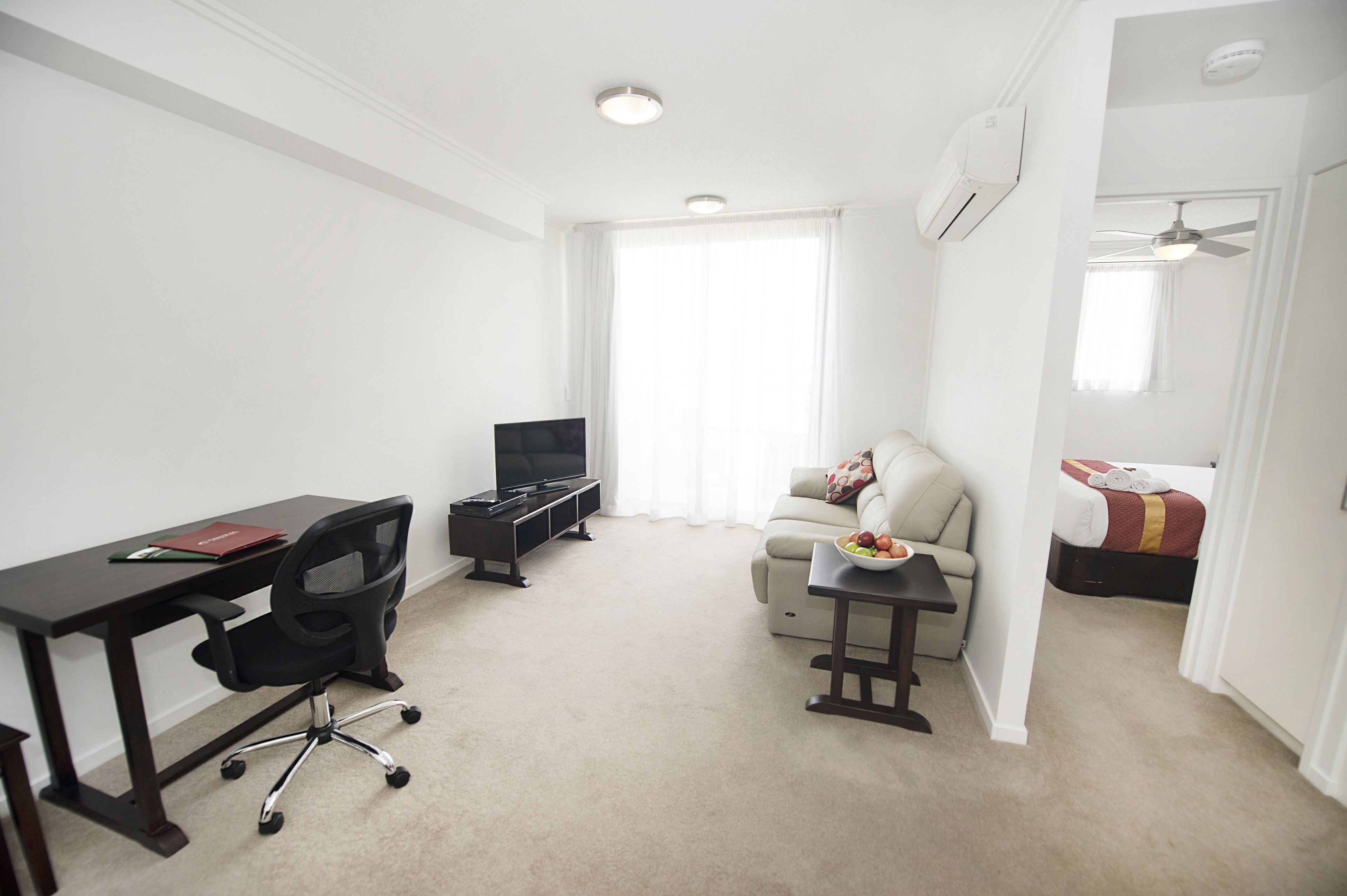 A living room with a desk, a sofa, a television, and a ceiling fan.