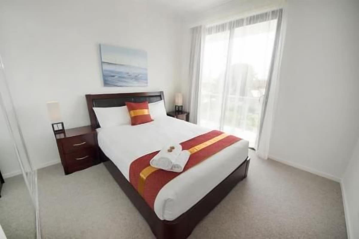 A hotel room with a large bed, a nightstand, a lamp, and a window with curtains.
