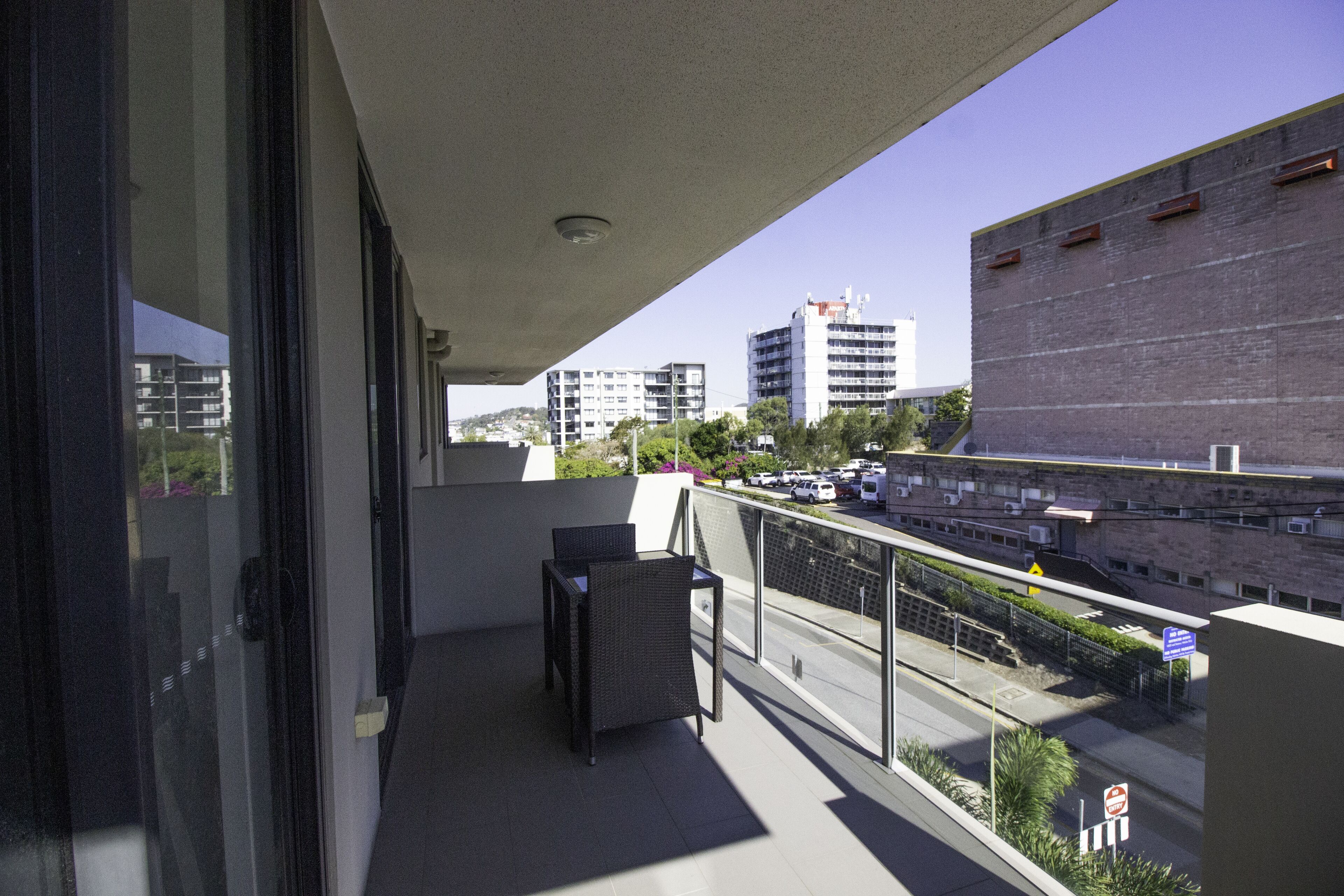 Un balcon avec deux fauteuils en osier, une vue sur une rue animée et des bâtiments en arrière-plan.