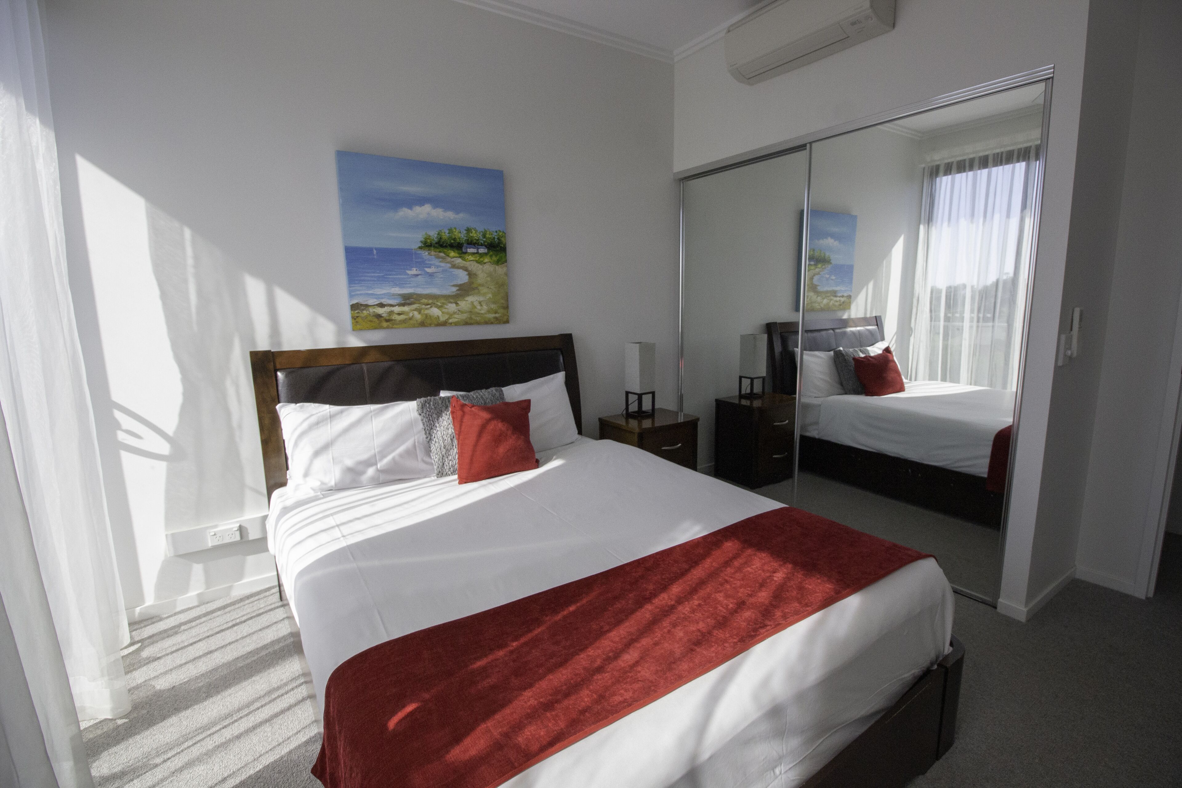 Een hotelkamer met een groot bed, een nachtkastje, een spiegel en een schilderij van een strandlandschap.