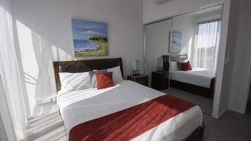 Een hotelkamer met een groot bed, een nachtkastje, een spiegel en een schilderij van een strandlandschap.