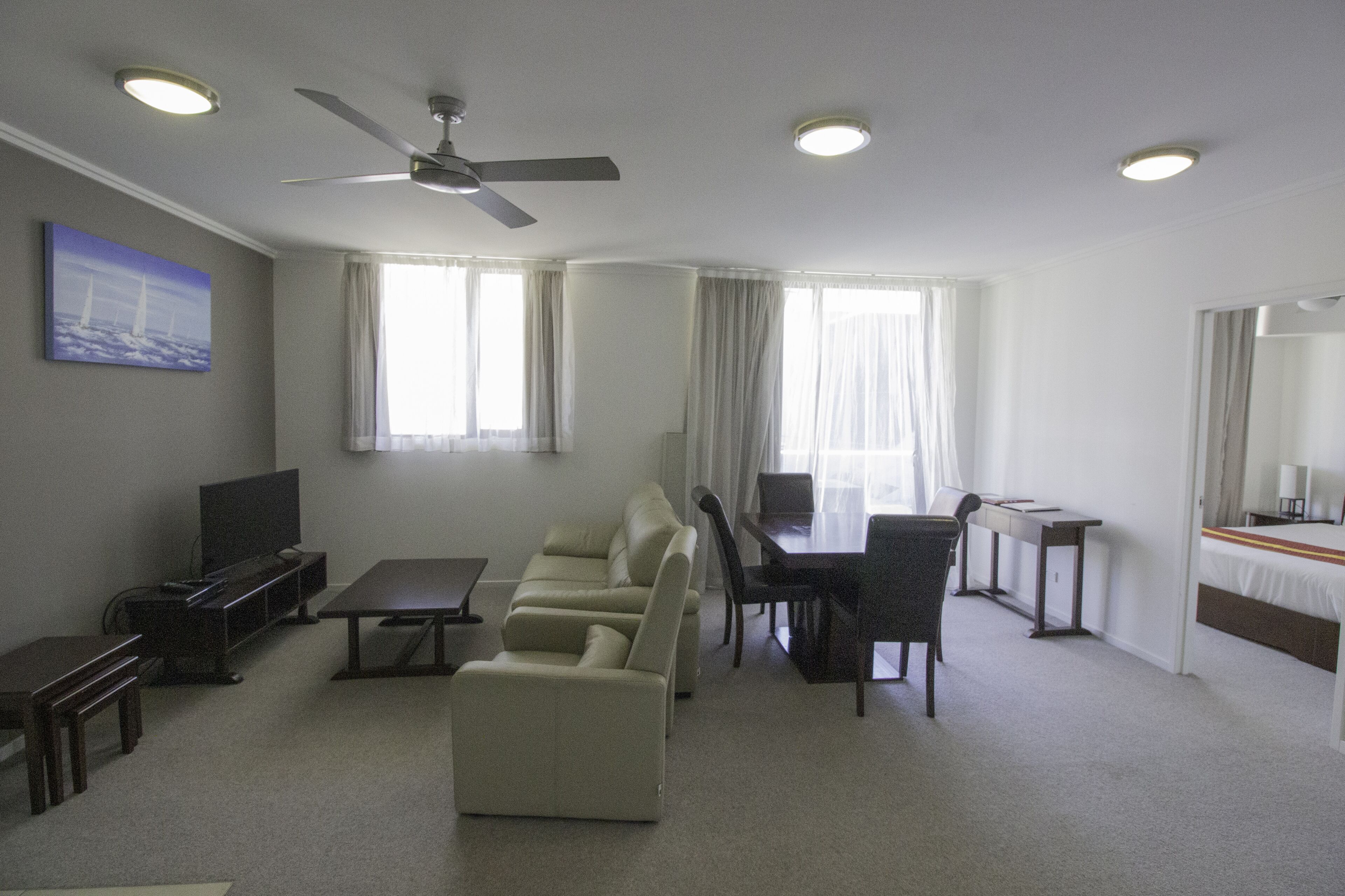 A hotel room with a sofa, a dining table, a TV, and a ceiling fan.