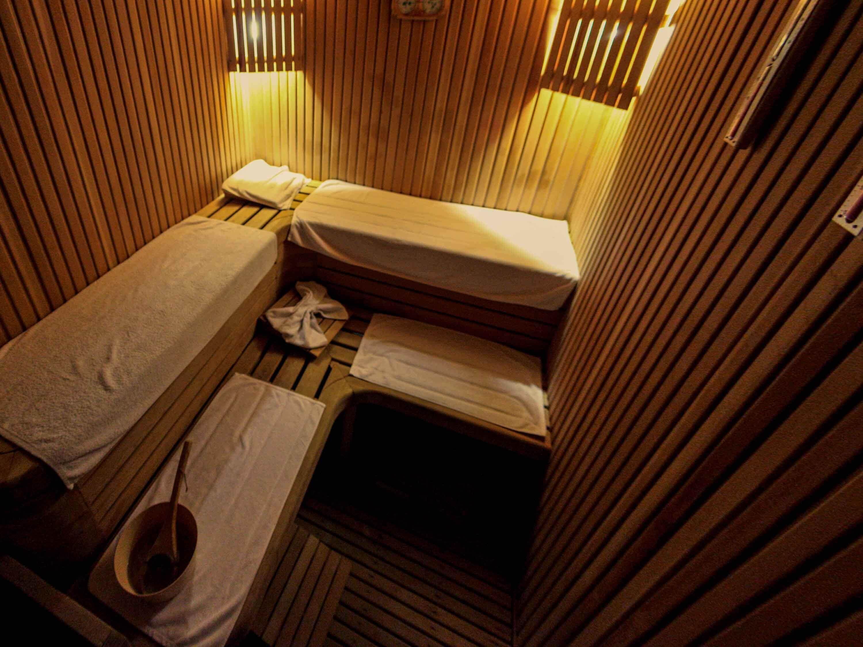 Una stanza sauna con listelli di legno, due panche, asciugamani e un secchio di legno.