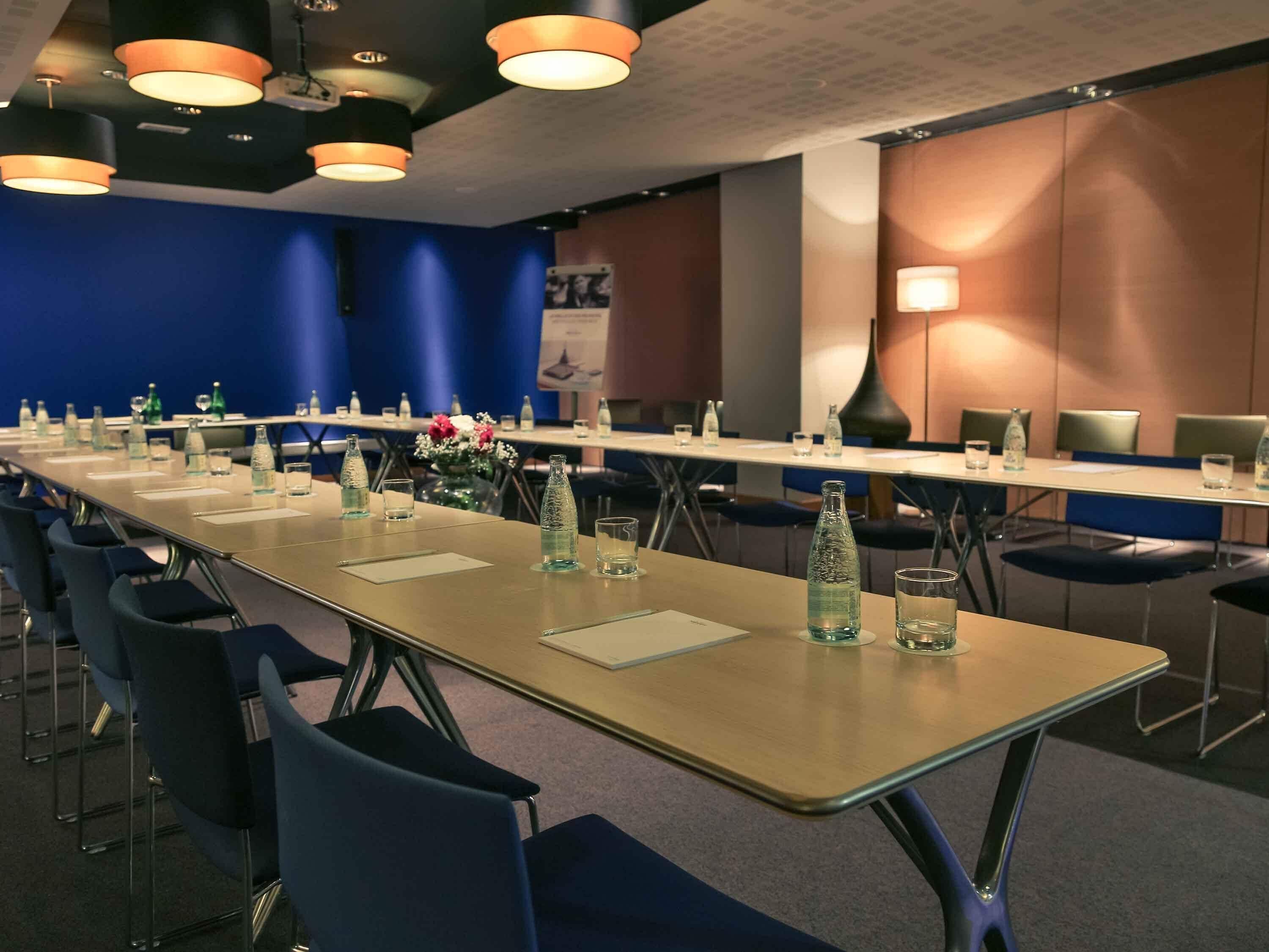 A conference room with a long table, chairs, water bottles, and a vase of flowers.