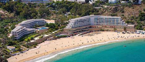 A coastal hotel with multiple buildings, a beach, and a view of the city in the background.