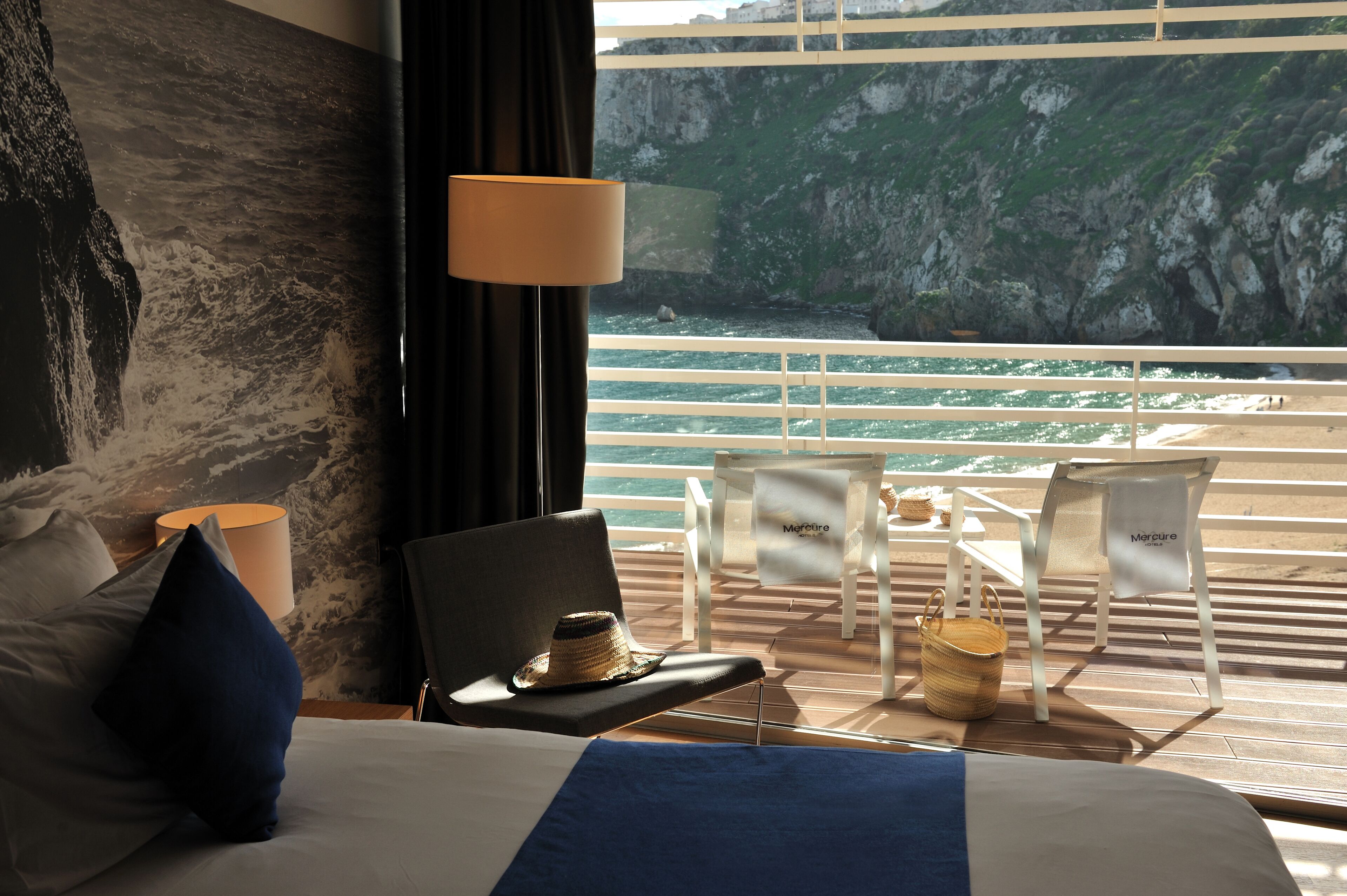 Une chambre d’hôtel avec un lit, une chaise, une table et une vue sur l’océan et les falaises.