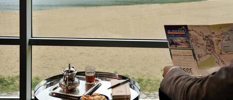 A table with a tray containing a teapot, a glass of tea, and pastries, with a map of Al Hoceima city in the foreground.