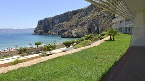 A balcony with a view of a coastal landscape, including a grassy area, a stone pathway, and a building with a sloped roof. - Mercure Quemado Resort (Al Hoceima)