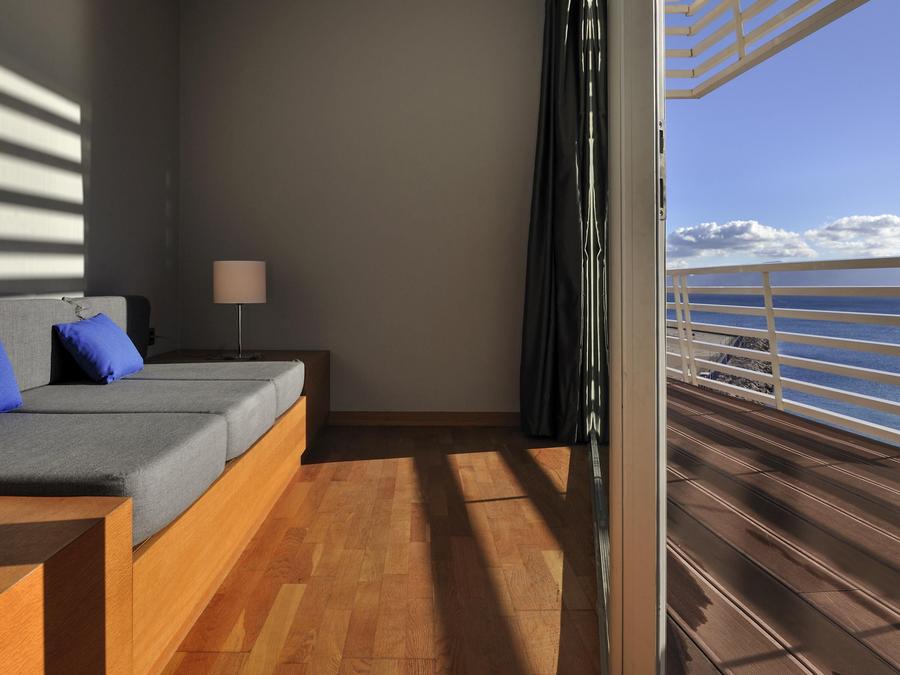 Un balcon doté d’un plancher en bois et d’une balustrade, offrant une vue sur une étendue d’eau et les nuages.