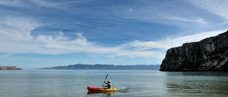 A kayaker in a red kayak on calm water with a clear sky and distant mountains.