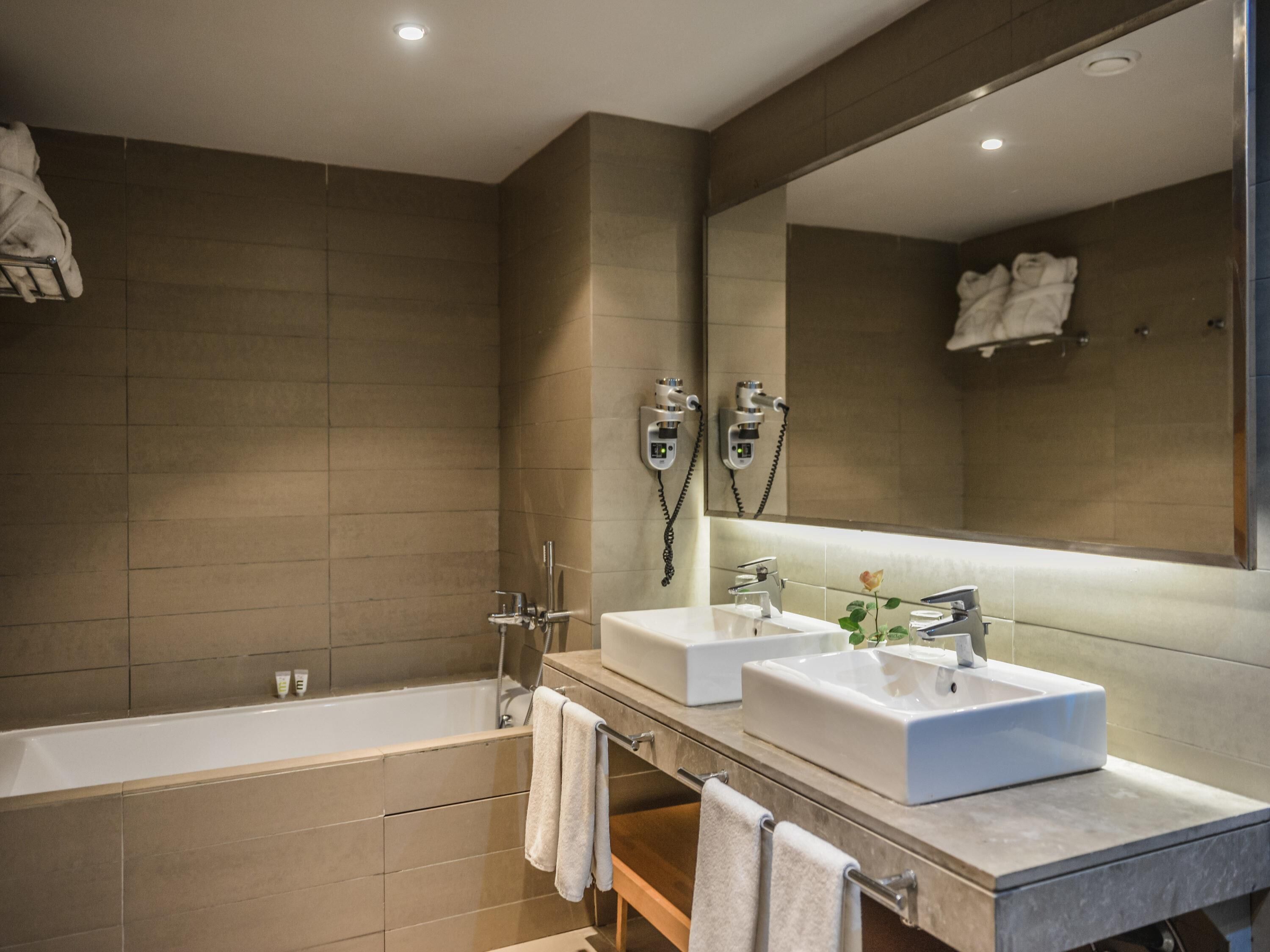 Une salle de bain moderne avec deux lavabos, une baignoire et un grand miroir.