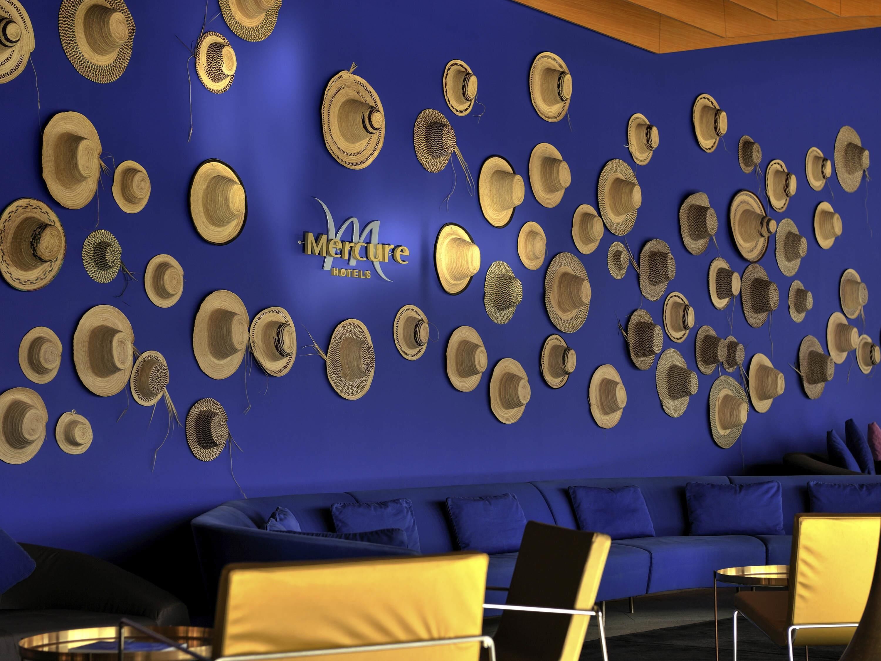 Un hall d’hôtel avec un mur bleu orné de nombreux chapeaux tissés et une enseigne « Mercure Hotels ».