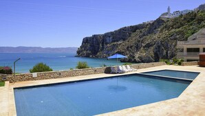A swimming pool with lounge chairs, a stone wall, and a view of the sea and mountains. - Mercure Quemado Resort (Al Hoceima)