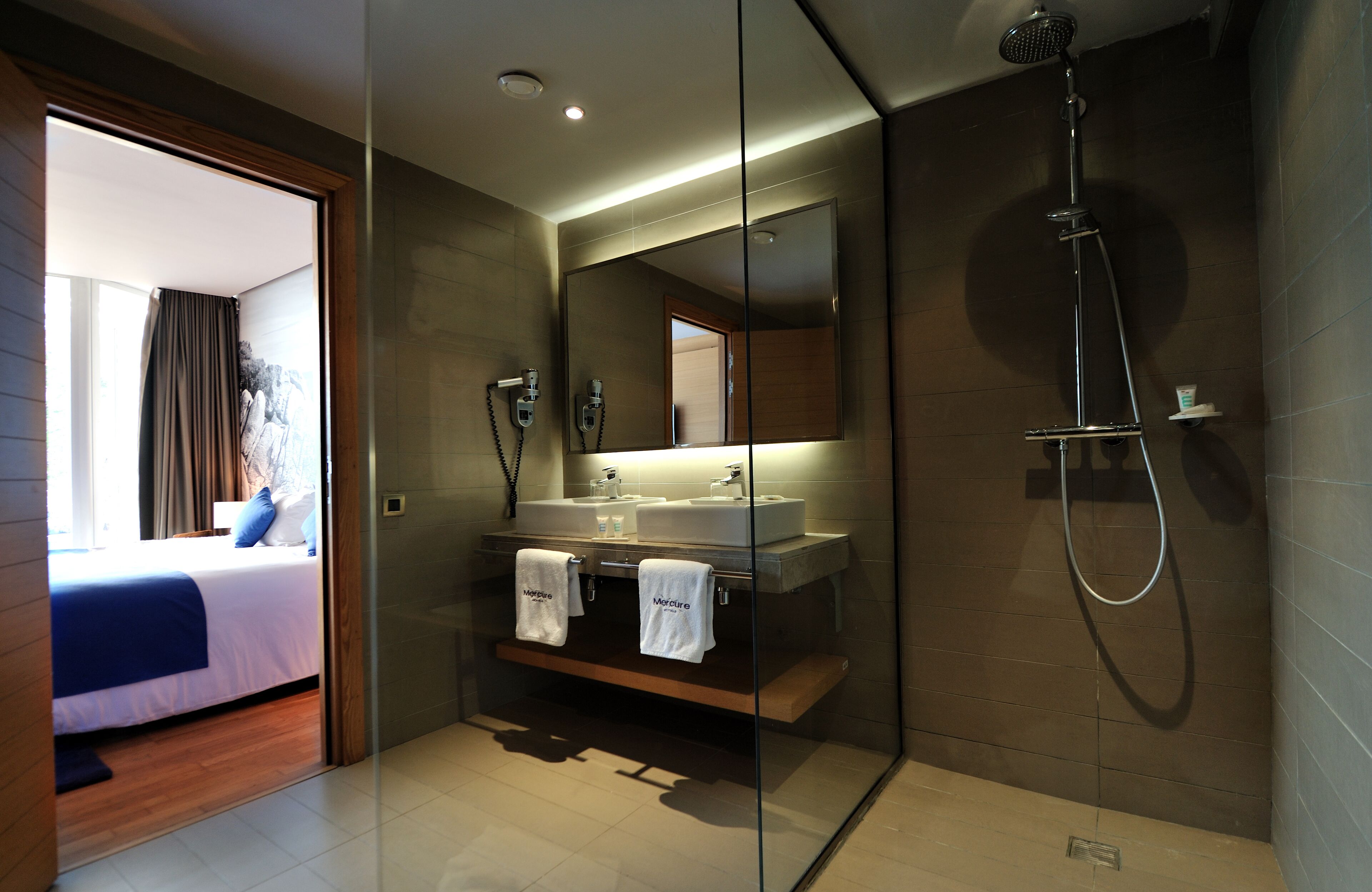 Une salle de bain moderne dotée d’une douche à parois de verre, d’un grand miroir et d’un meuble-lavabo à deux vasques.
