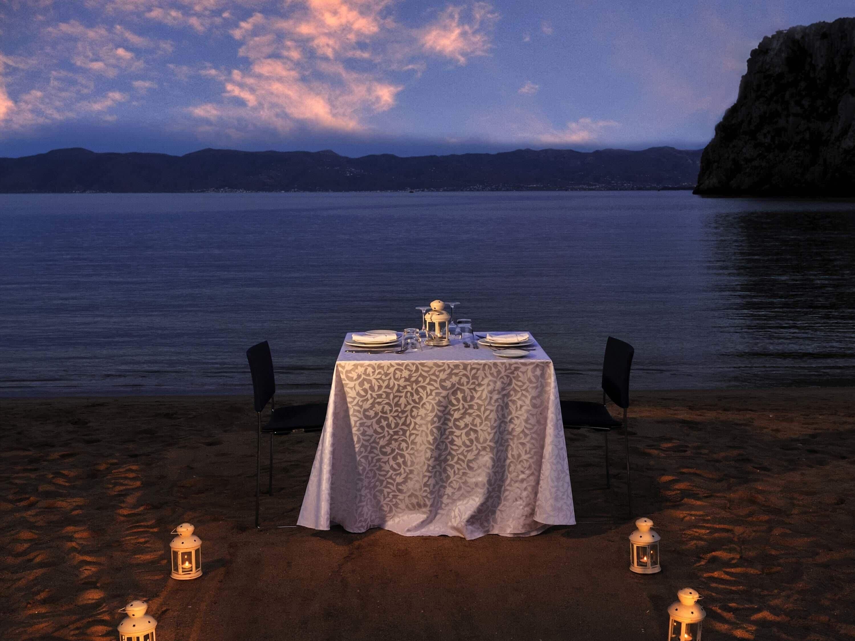 Une table dressée pour deux personnes, avec vue sur la mer et les montagnes en arrière-plan.