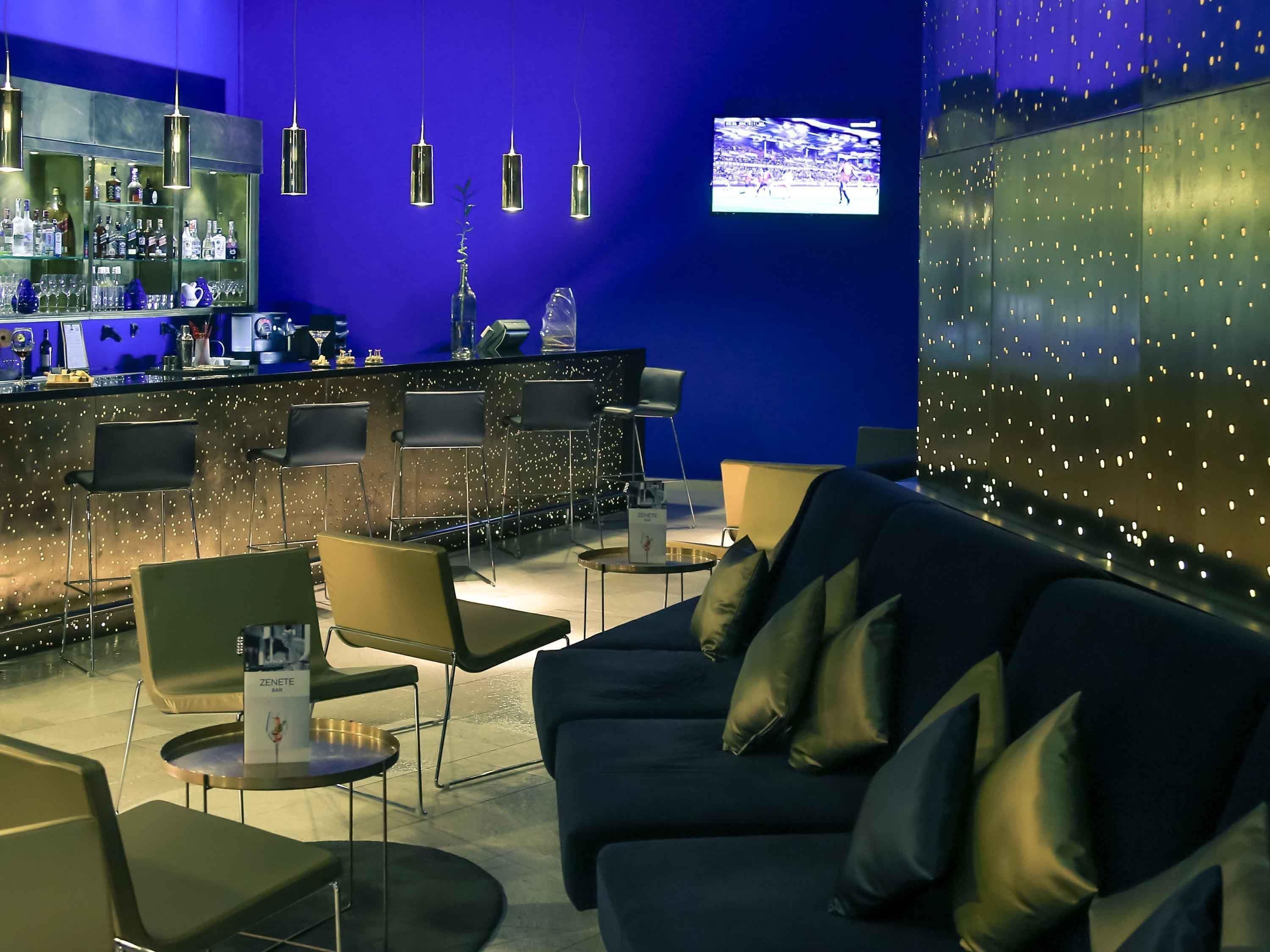 A bar area with a blue wall, hanging lights, and a television screen.