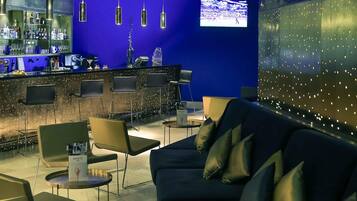 A bar area with a blue wall, hanging lights, and a television screen.