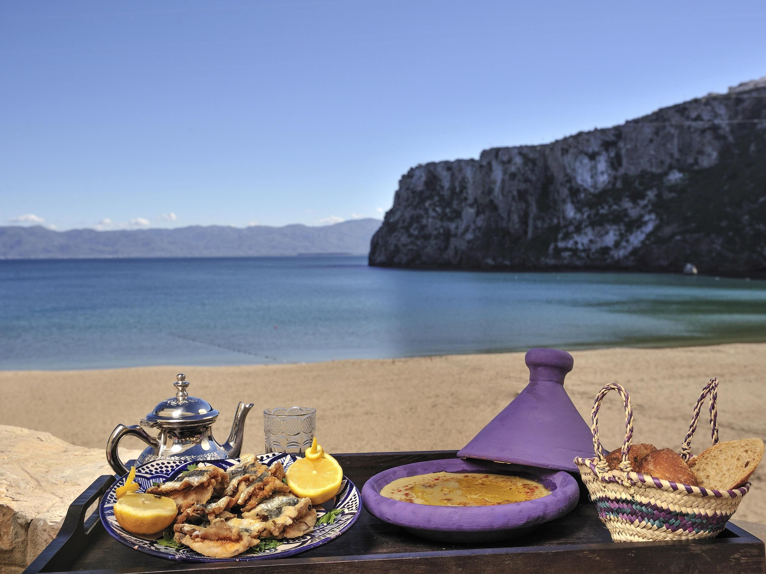 A tray of food and drinks on a table with a view of a coastal landscape.